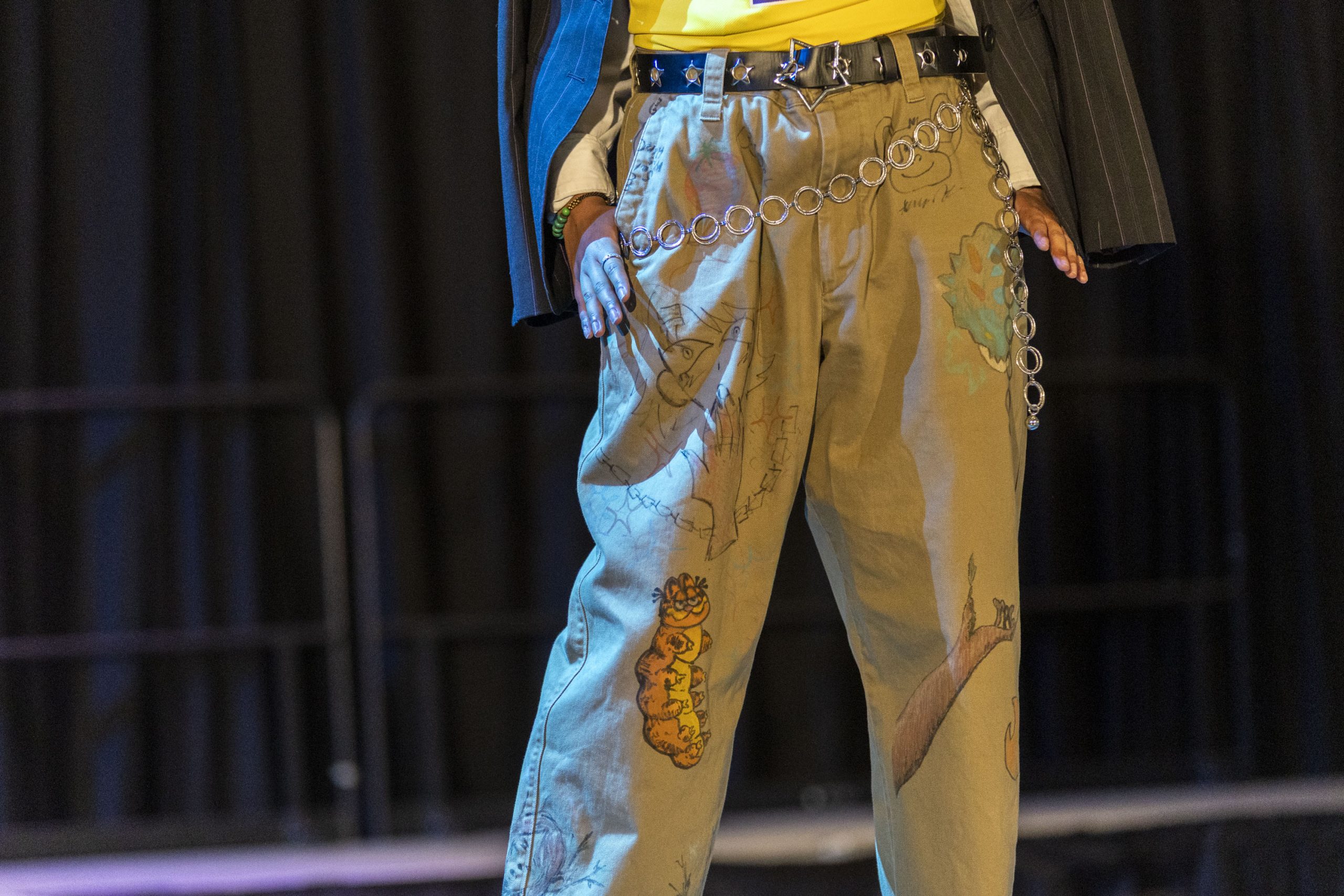 Person wearing illustrated brown pants with a chain belt on stage.