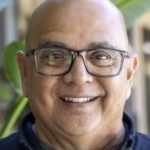 A man smiles in front of a large green plant leaf.